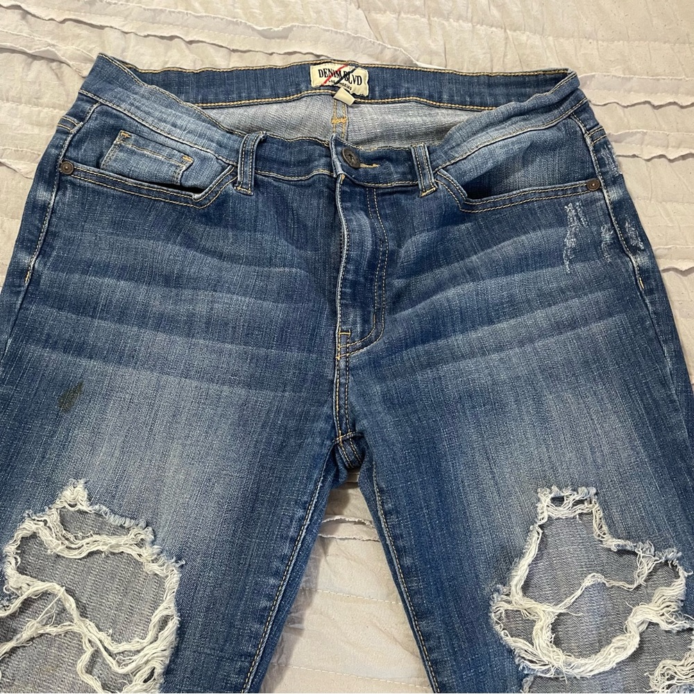 A pair of used Denim Blvd blue jeans with holes. The jeans are used.